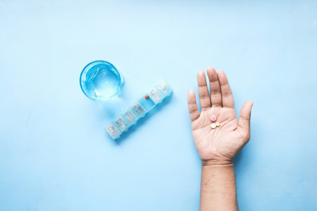 Pohľad na pohár, dávkovač na tabletky a ruku na ktorej sú antibiotiká, ktoré sú nadmerne užívané. 